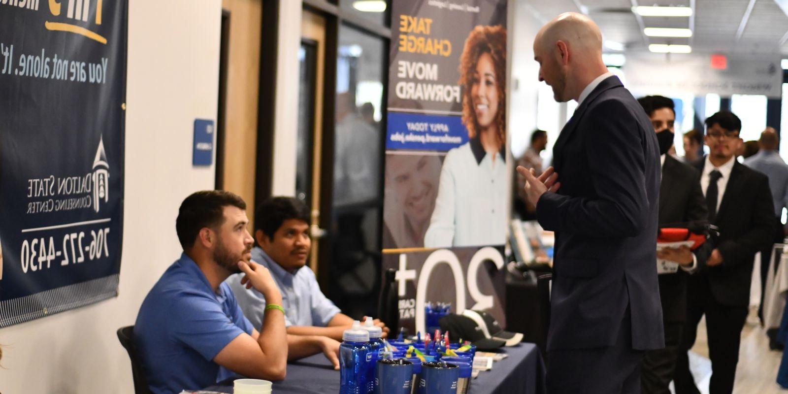 Student in suit in discussion with booth workers at event