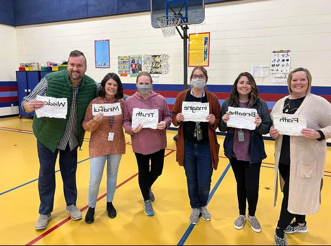 Teachers in a gym holding signs that say 