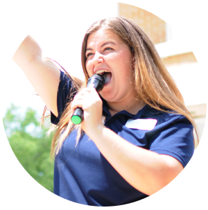 Woman with name tag and microphone, yelling and holding a hand up to the crowd